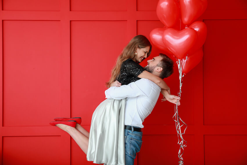 Woman holding heart-shaped balloons while being carried