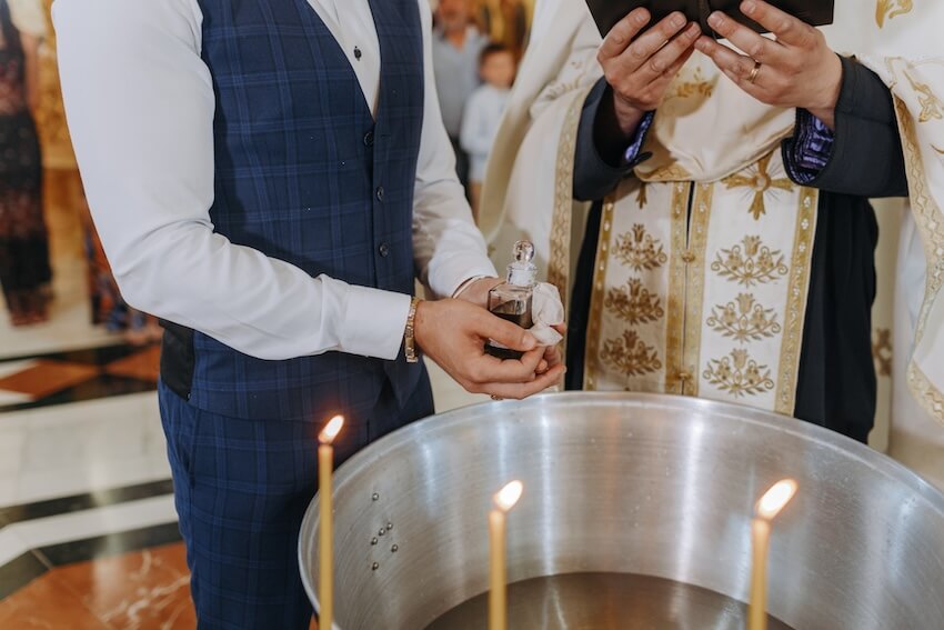 Baptism gifts for boys: man holding a small bottle while standing beside a priest and a baptismal font