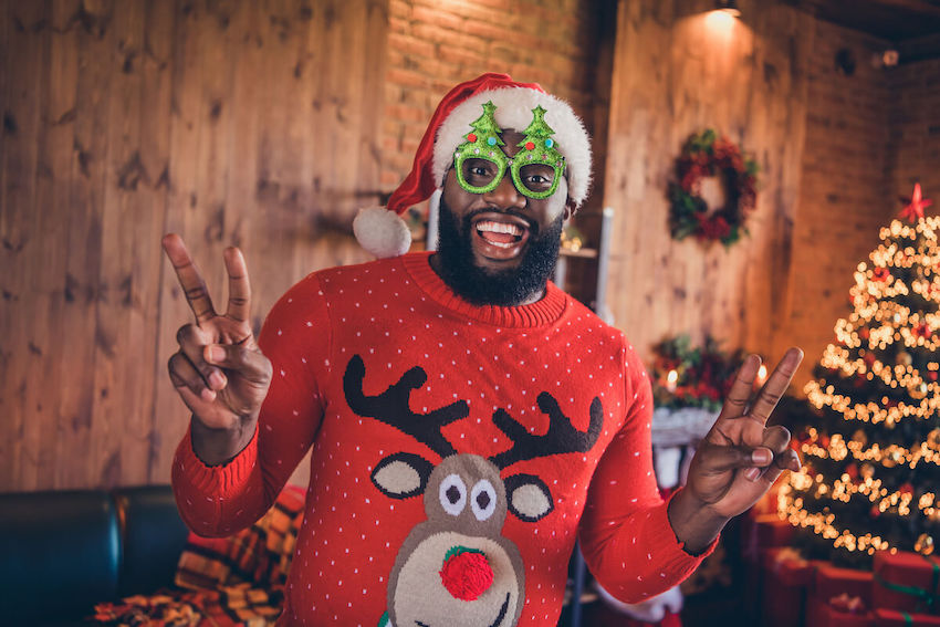 Ugly sweater party ideas: man smiling at the camera and doing the peace sign