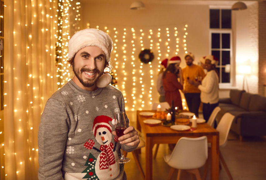 Ugly sweater party ideas: man smiling at the camera and holding a champagne glass