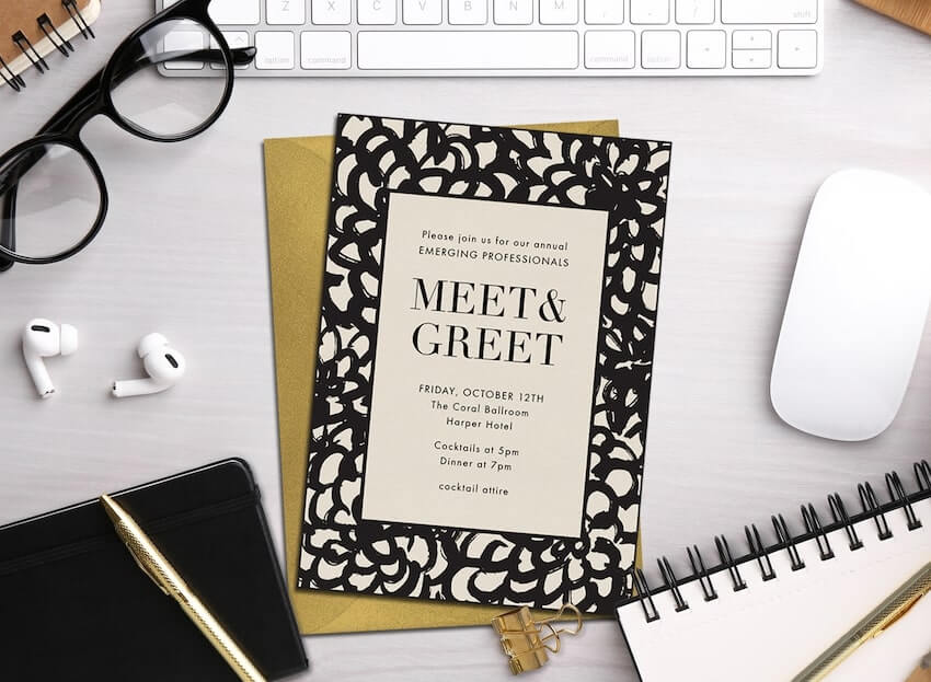 Meet and greet invitation, a computer mouse, a notebook, two pens, and a pair of eyeglasses on a desk