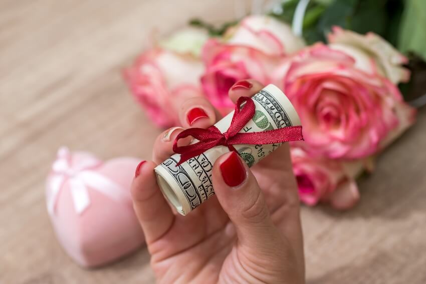 Money gift ideas for birthdays: person holding a bundle of bills with a red ribbon