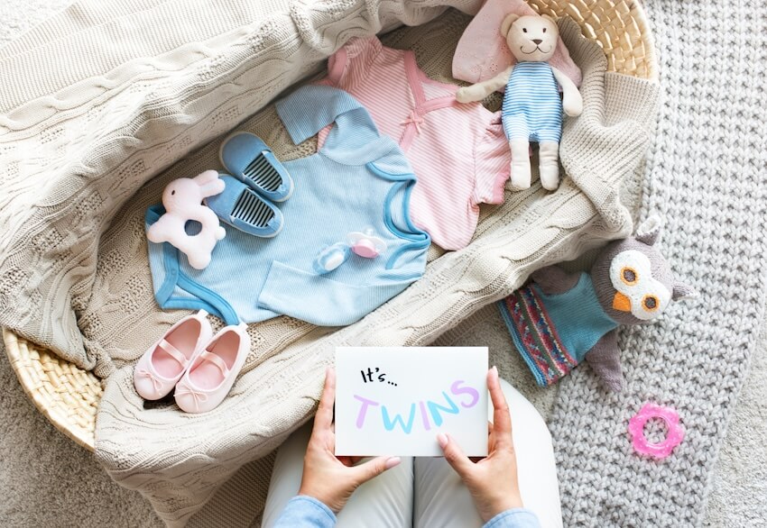 Twins baby shower invitations: person holding a card that says "It’s TWINS" and a basket filled with baby items