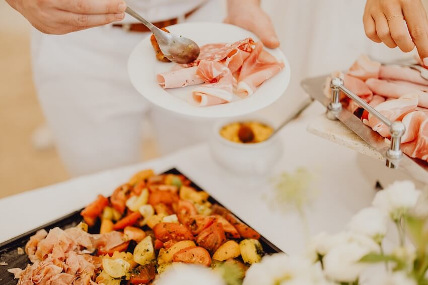 Brunch wedding: person placing slices of prosciutto on his plate