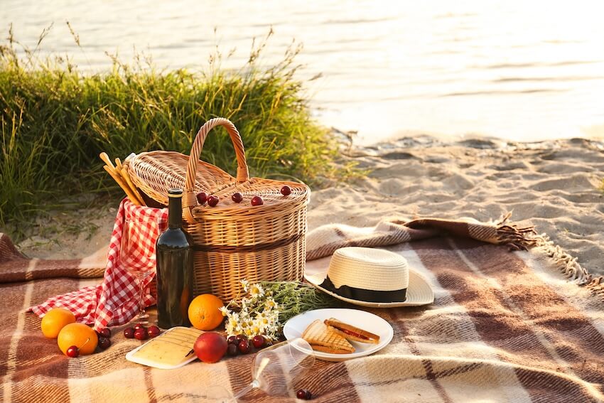 Basket, various food, and a hat on a picnic blanket