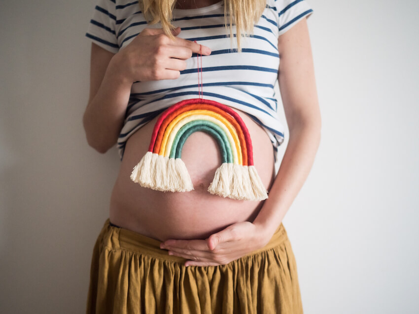 Rainbow baby announcement: pregnant woman holding a rainbow decoration