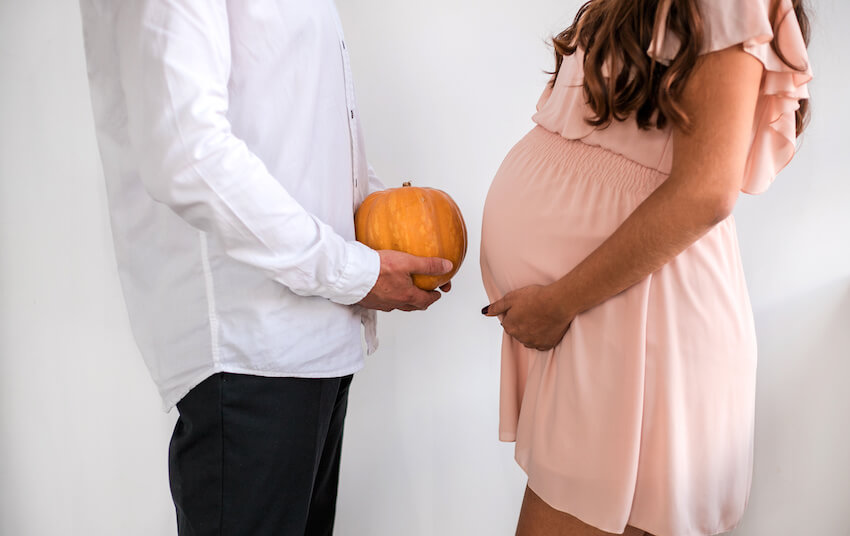 Fall pregnancy announcement: pregnant woman holding her belly and a man holding a pumpkin