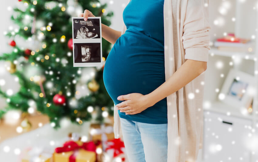 Winter pregnancy announcement: pregnant woman holding pictures of her baby's ultrasound