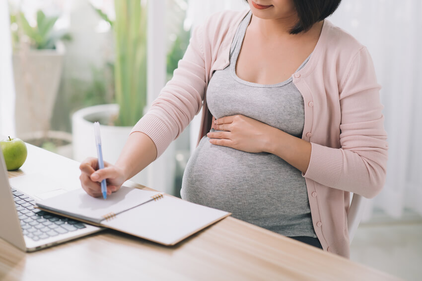 How to plan a baby shower: pregnant woman writing on a notebook