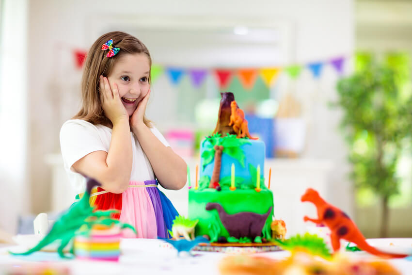 Dinosaur decorations: surprised girl looking at a dinosaur themed cake on a table