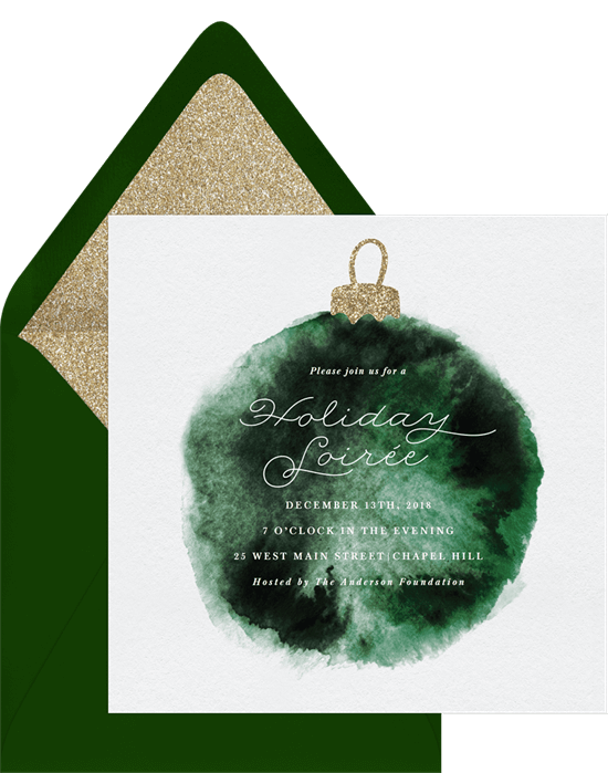 A holiday invitation with a green watercolored ornament, with a matching green envelope with sparkly gold liner
