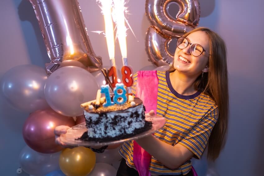 Happy 18th birthday daughter: woman holding her cake with two number 18 candles on top of her cake