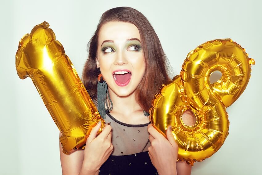 18th birthday wishes: woman holding up a set of golden number 18 balloons