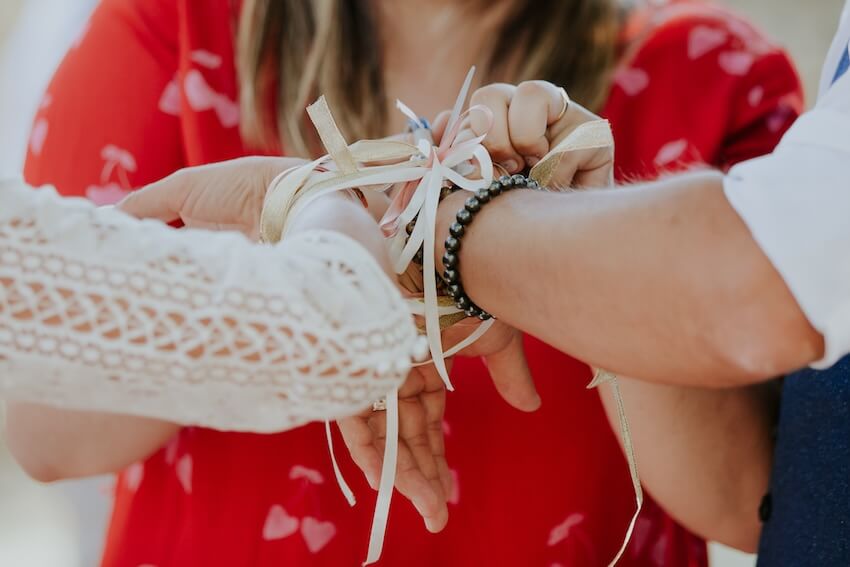 Woman using a ribbon to tie a couple’s hands together