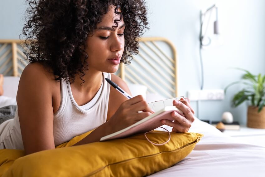 30th birthday gift ideas: woman writing in a notebook while lying in bed